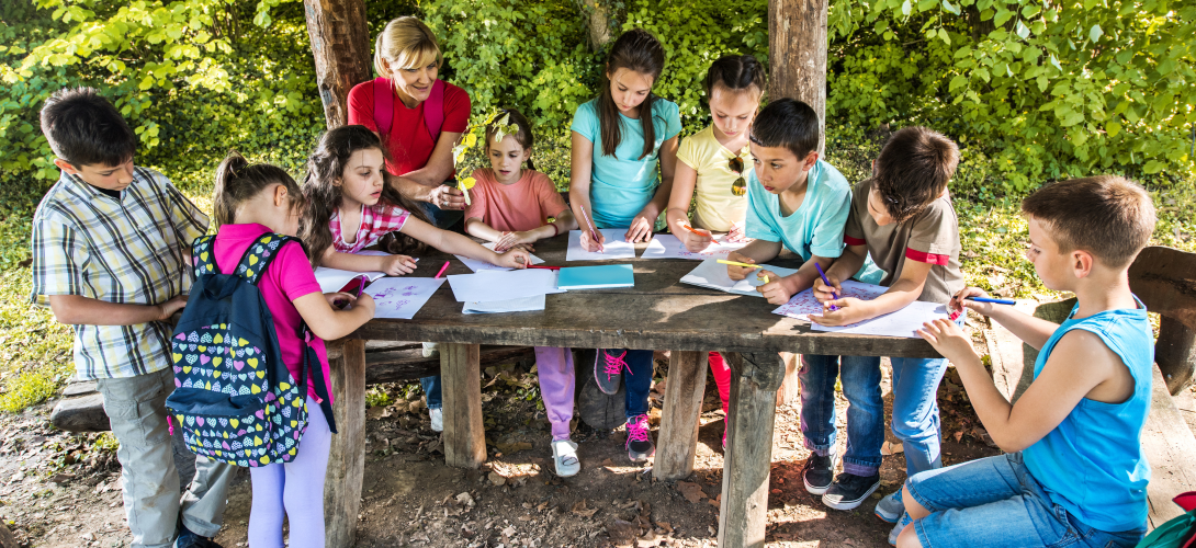 School kids colouring on a field trip with their teacher.
