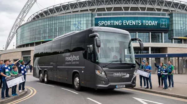 A wide landscape photograph of a metallic charcoal-grey Readybus executive coach parked on an asphalt road outside a large, modern sports stadium. Groups of sports fans wearing blue and green team colors stand on the sidewalks nearby.